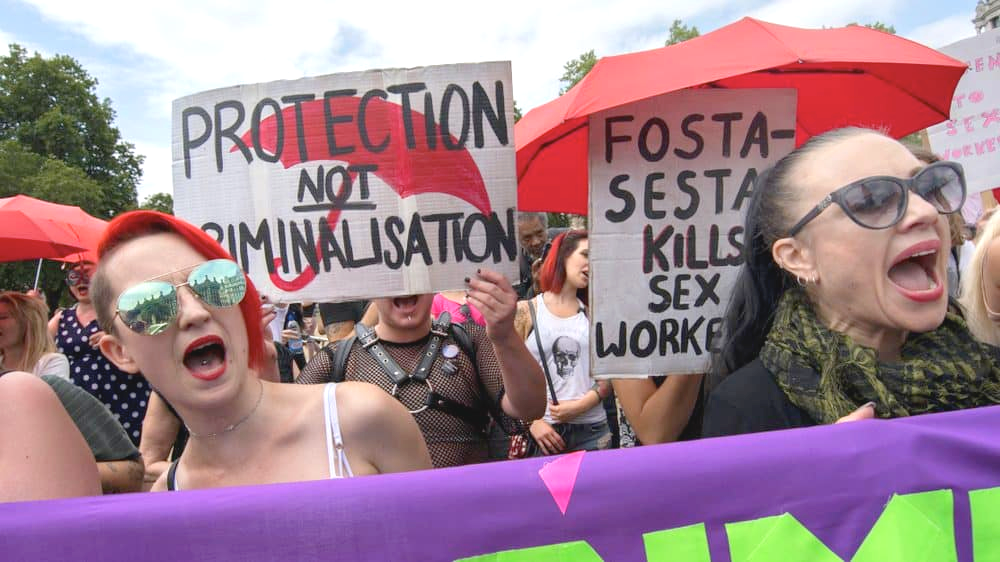 Image of protesters holding signs and a red umbrella. Signs read "Protection Not Criminalization" and "FOSTA-SESTA Kills Sex Workers"