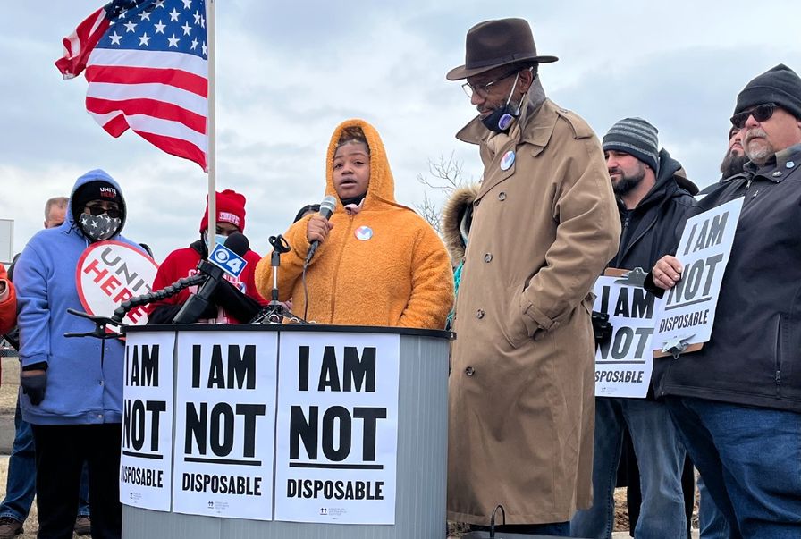 Thumbnail image of woman speaking into a microphone at an Amazon protest. She's standing at a podium adorned with signs that say "I am NOT disposable."