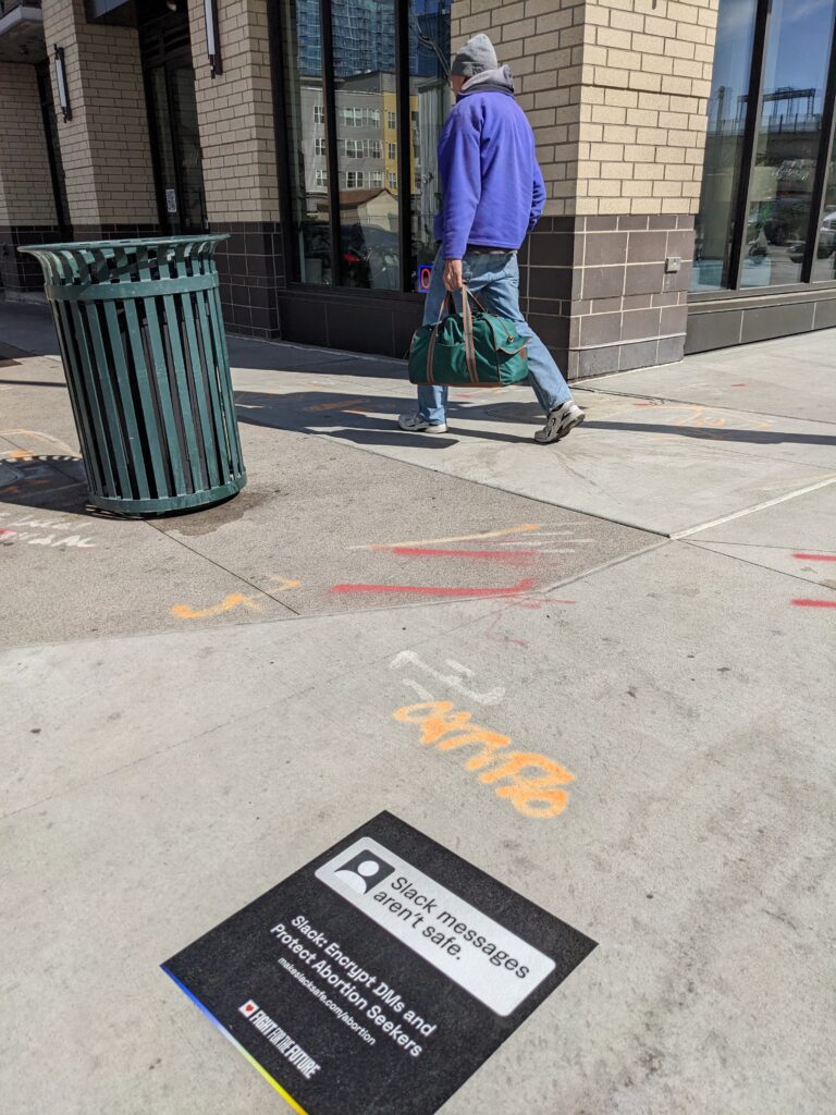 Sidewalk decal with text "Slack Messages Aren't Safe. Slack: Encrypt DMs and Protect Abortion Seekers makeslacksafe.com/abortion"