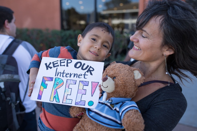 A woman holding a child who is holding a sign that says "Keep our Internet FREE!"