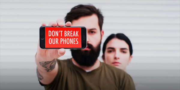 Man holding a phone that displays the image "Don't Break Our Phones", woman standing behind him