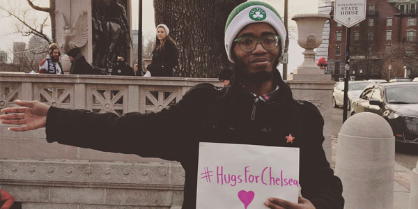 Man offering a hug to Chelsea with a poster that says "#HugsForChelsea <3"